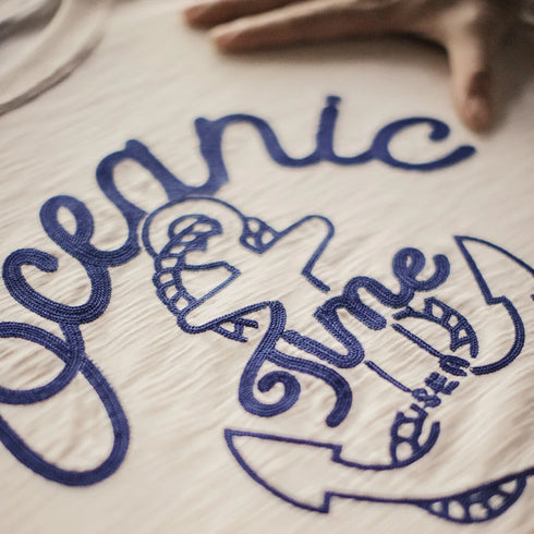 Close-up of a shirt with blue embroidered text and graphics on a beige background.